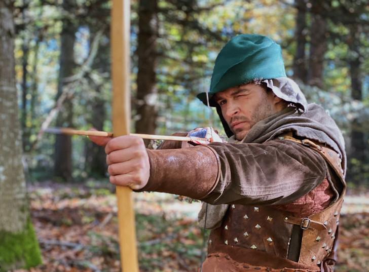 Un comédien interprétant le rôle de Robin des Bois prêt à dégainer une flèche